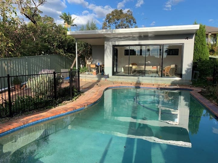 Black aluminium pool fence running behind a curved pool towards a garden studio