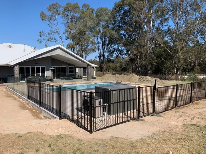 Black flat-top aluminium pool fence around a newly built pool beside a single-storey home