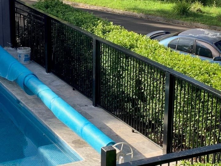 Close view of black aluminium fence panels and posts between a pool and a clipped hedge