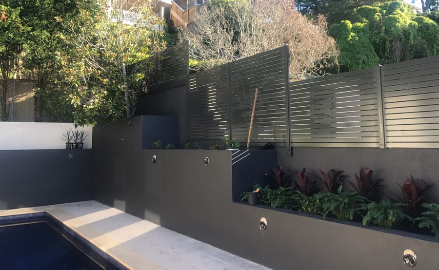 Charcoal aluminium slat screens stepping up a terraced garden wall above a pool