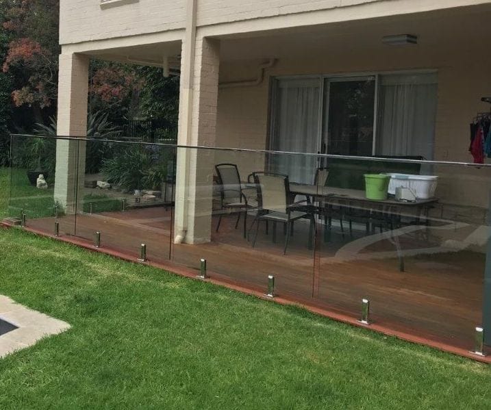 Glass balustrade on stainless fittings along the edge of a timber deck beside a lawn
