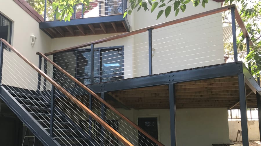 Wire balustrade with a timber handrail along a raised deck and external stair, with charcoal posts
