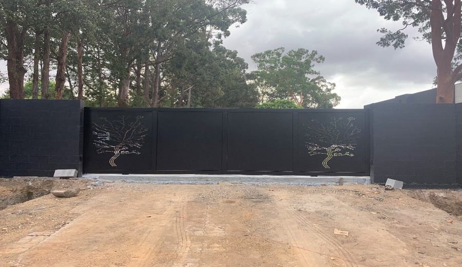Black driveway gate with two cut-pattern decorative tree panels, between black rendered piers