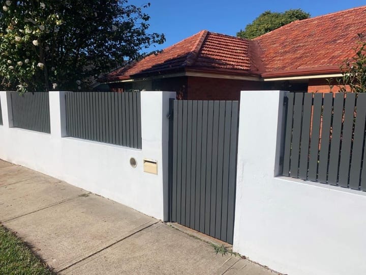 Grey vertical slat infills and a matching pedestrian gate set between white rendered piers on a front wall