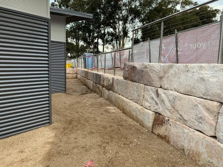 Dark grey louvre screen on the side of a building next to a sandstone block retaining wall