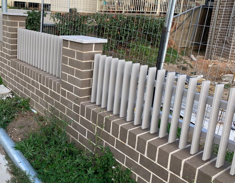 Pale aluminium picket infills set between brick piers on a low brick front wall