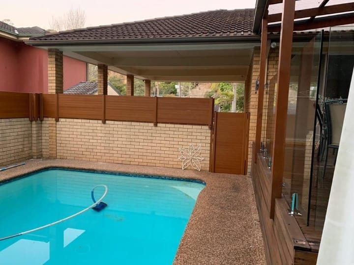 Slat privacy screen along the back of a pool area beside a brick wall
