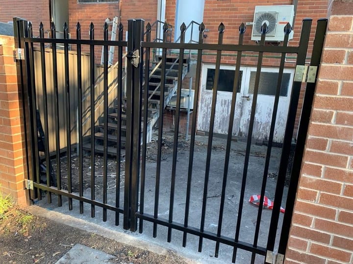 Pair of black spear-top swing gates closing an opening between brick walls